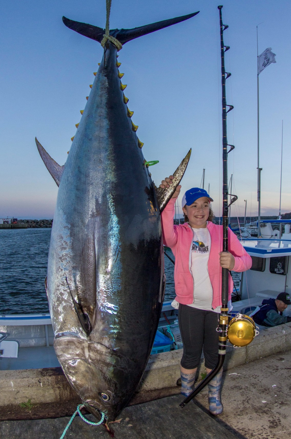 Young angler dwarfed by a giant bluefin tuna hanging dockside