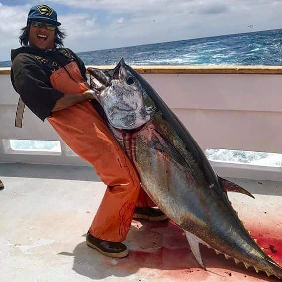 Angler bear-hugging a chunky yellowfin in orange foulies